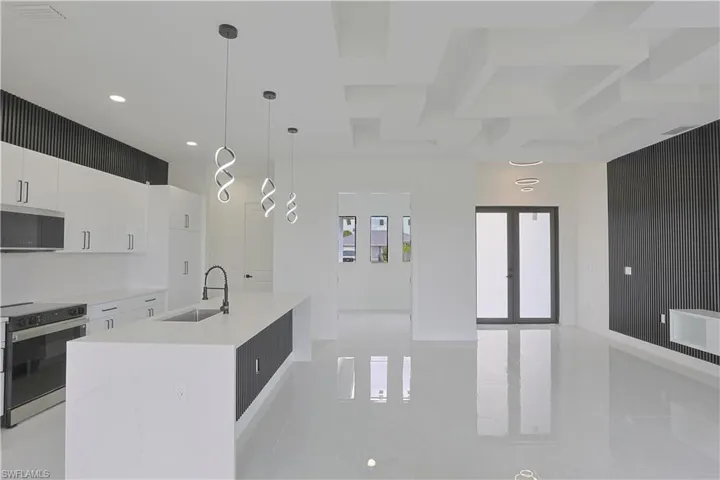 Kitchen featuring light countertops, white cabinets, range with electric cooktop, an island with sink, and a sink