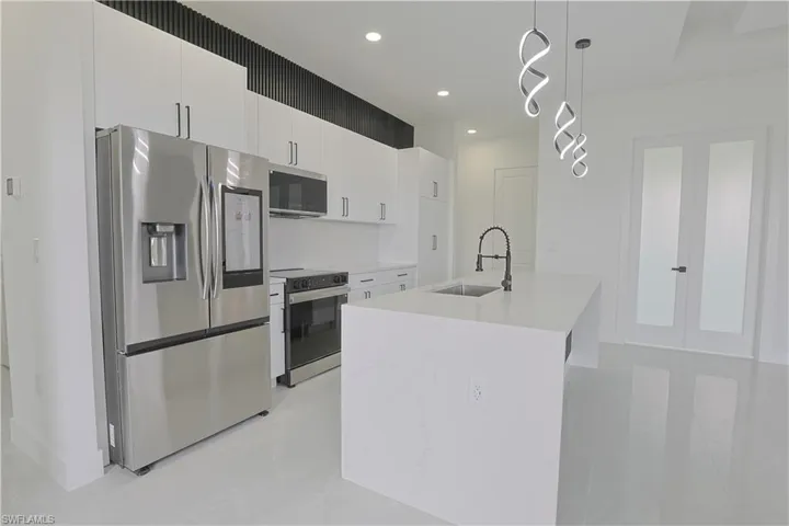 Kitchen with white cabinets, light countertops, stainless steel appliances, a sink, and pendant lighting