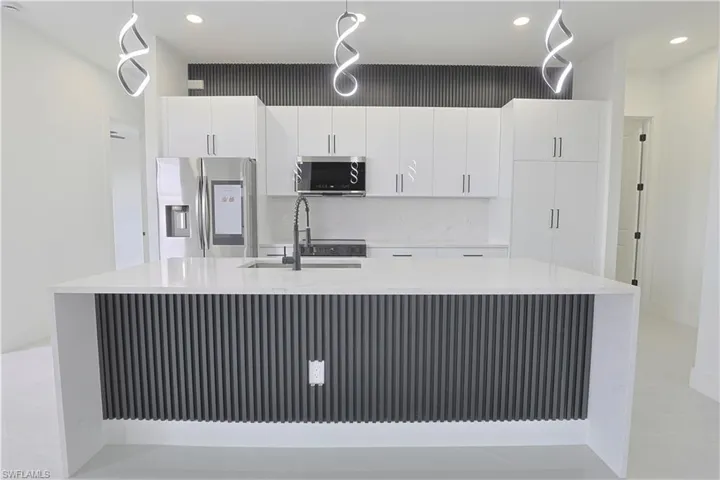 Kitchen featuring light countertops, a center island with sink, appliances with stainless steel finishes, white cabinetry, and a sink