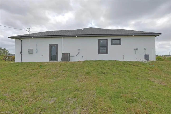 Back of house with a lawn, central AC unit, and stucco siding