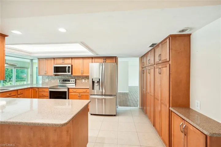Kitchen with appliances with stainless steel finishes, kitchen peninsula, light tile patterned floors, and light stone counters