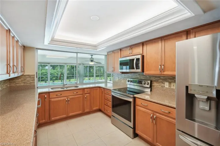 Kitchen featuring tasteful backsplash, stainless steel appliances, a tray ceiling, ceiling fan, and sink