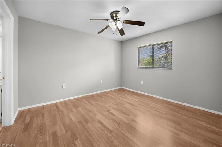 Bedroom featuring wood-finish flooring, a ceiling fan with integrated lighting, and a window with exterior tree scenery