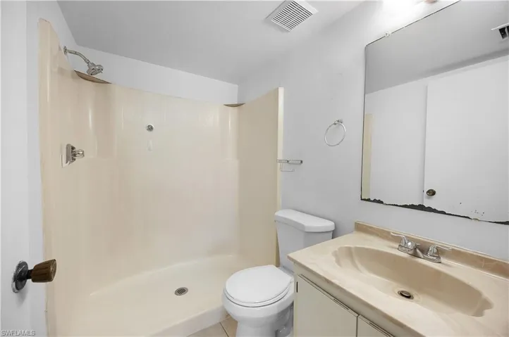 Bathroom featuring a shower stall with integrated shelving, a single vanity with a light-toned countertop and integrated sink, a wall-mounted mirror, and a toilet
