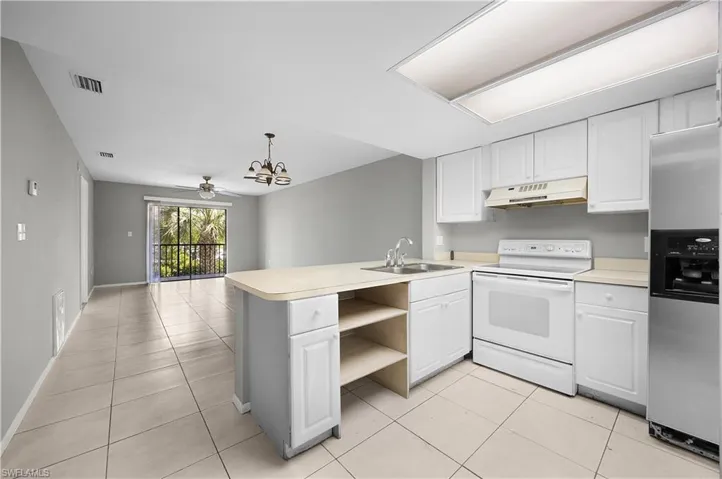Open-concept kitchen and living area featuring white cabinetry, light-toned tile flooring, and a kitchen island with integrated sink