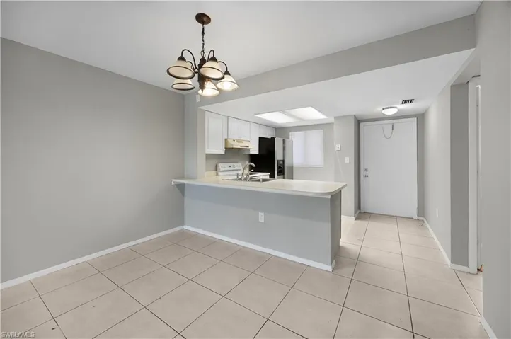 Open-concept living area featuring a kitchen with white cabinetry and appliances, a breakfast bar, and tile flooring