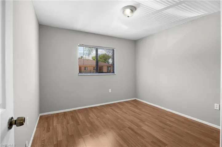Room featuring wood-finish flooring, light grey painted walls, a window with horizontal blinds, a white ceiling, and a flush-mount ceiling light fixture