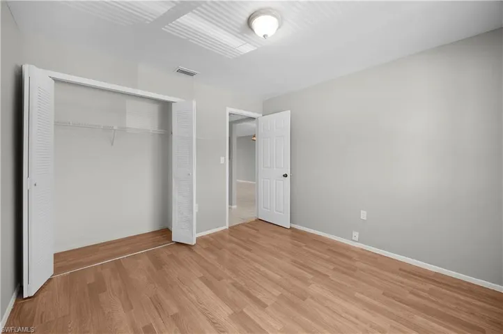 Spacious room featuring wood-finish flooring, light grey painted walls, and a ceiling-mounted light fixture