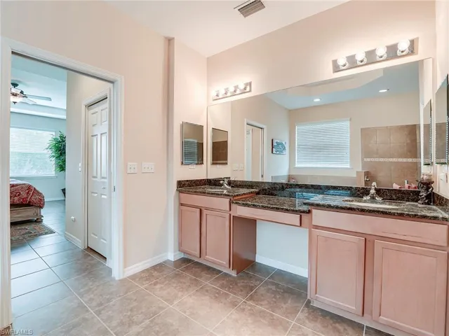Ensuite bathroom with double vanity, light tile patterned flooring, and ceiling fan