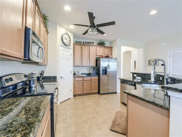 Kitchen with appliances with stainless steel finishes, dark stone counters, arched walkways, recessed lighting, and a ceiling fan