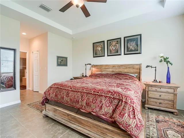 Tiled bedroom featuring a raised ceiling, a ceiling fan, ensuite bathroom, and recessed lighting