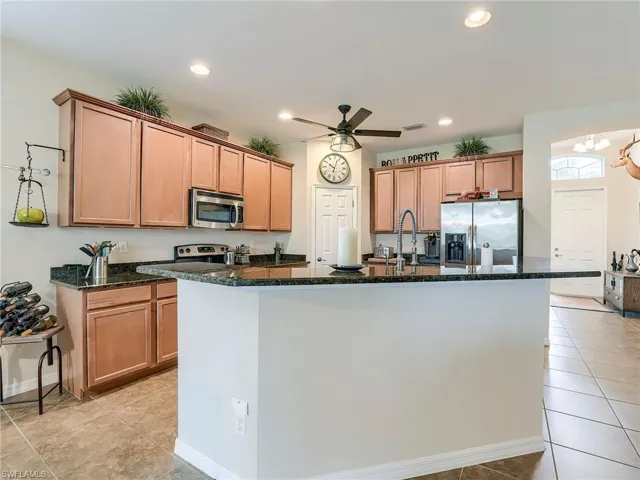 Kitchen with appliances with stainless steel finishes, dark stone countertops, a center island with sink, light tile patterned flooring, and brown cabinets