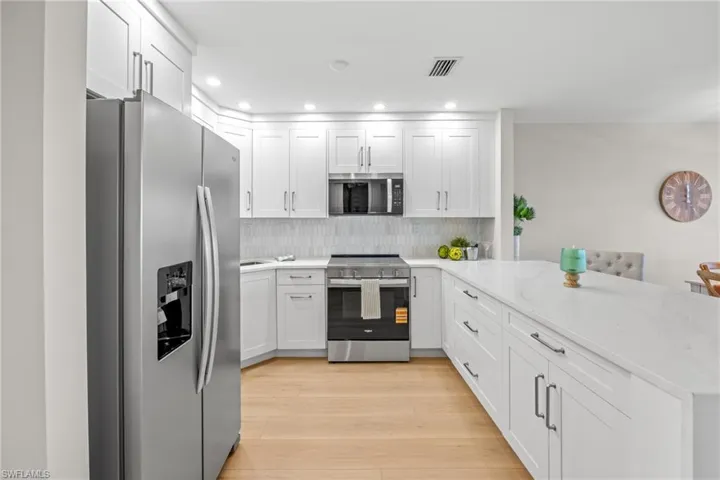 Kitchen featuring stainless steel appliances, light stone counters, a peninsula, white cabinets, and recessed lighting