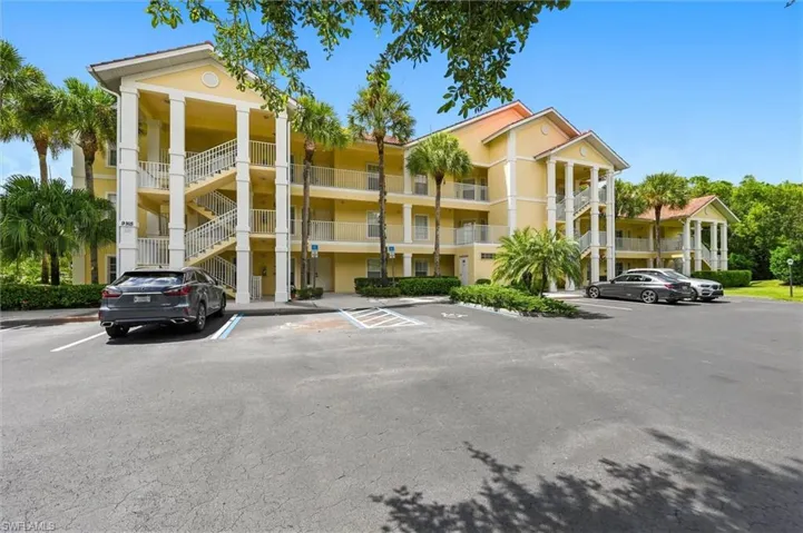 Multi-story residential building with a stucco exterior, multiple private balconies, and mature palm trees