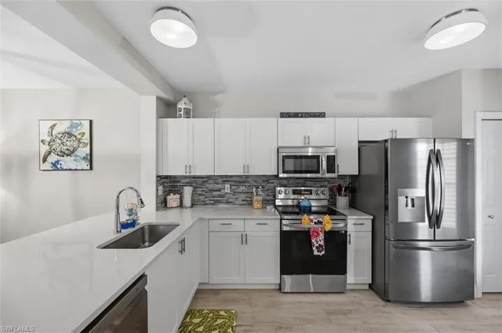 White cabinetry, light-toned countertops, stainless steel appliances, stainless steel sink, and wood-finish flooring