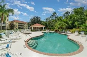 Community swimming pool with integrated steps, surrounding paved deck, screened gazebo, and lush perimeter landscaping