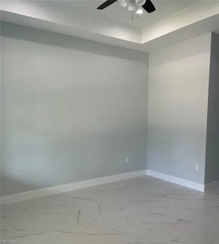 Tiled empty room featuring ceiling fan and a tray ceiling