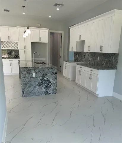 Kitchen with white cabinetry, tasteful backsplash, and an island with sink
