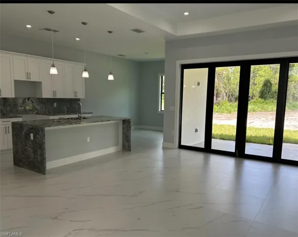 Kitchen featuring light tile patterned flooring, a wealth of natural light, tasteful backsplash, and white cabinetry