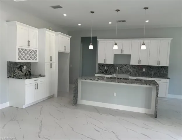 Kitchen featuring backsplash, a kitchen island with sink, white cabinetry, and pendant lighting