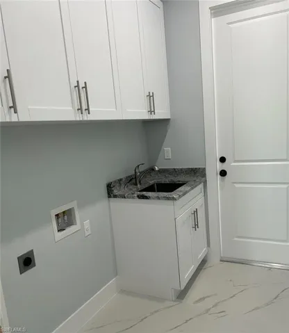 Laundry area with sink, washer hookup, cabinets, hookup for an electric dryer, and light tile patterned floors