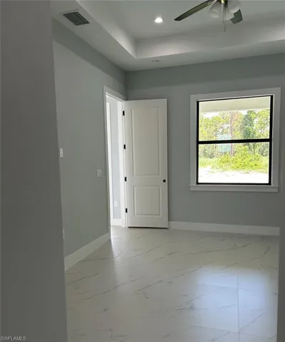 Tiled empty room featuring ceiling fan and a tray ceiling