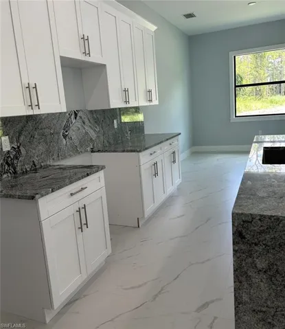 Kitchen with light tile patterned floors, dark stone countertops, decorative backsplash, and white cabinets