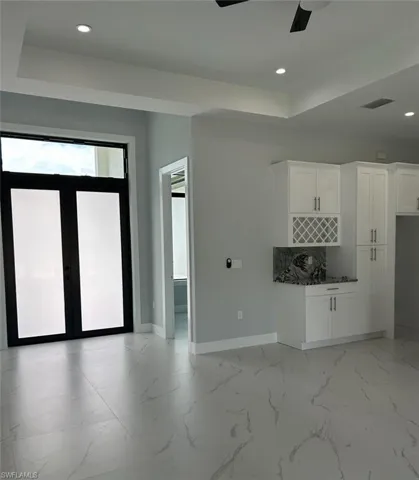 Kitchen featuring tasteful backsplash, a raised ceiling, white cabinets, light tile patterned floors, and ceiling fan