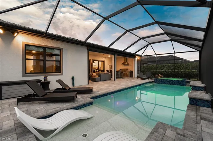 View of swimming pool featuring a screen enclosure, a patio area, a pool with connected hot tub, and outdoor lounge area