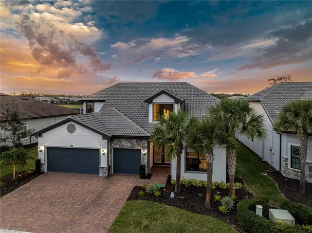 View of front facade with a tiled roof, stone siding, an attached garage, decorative driveway, and stucco siding
