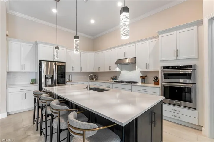 Kitchen featuring white cabinetry, tasteful backsplash, a center island with sink, appliances with stainless steel finishes, and crown molding