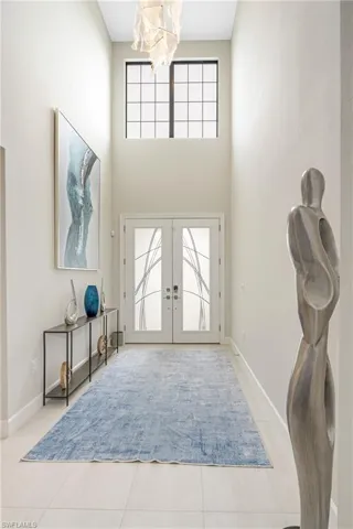 Entryway featuring french doors, a towering ceiling, light tile patterned flooring, and a chandelier