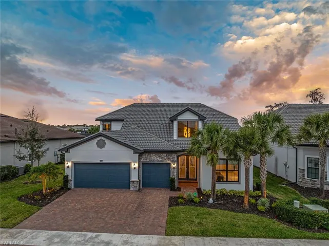 View of front of property featuring decorative driveway, an attached garage, stone siding, a front yard, and a tiled roof