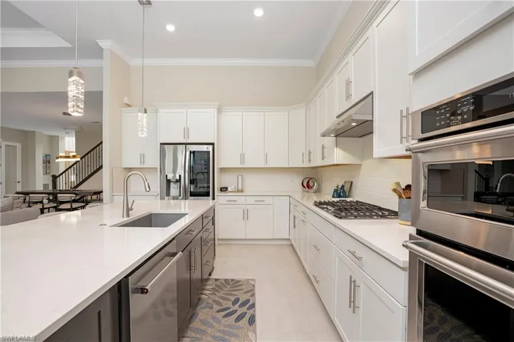 Kitchen with stainless steel appliances, white cabinets, crown molding, pendant lighting, and tasteful backsplash