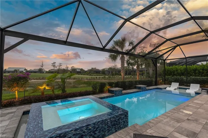 Pool at dusk featuring screen enclosure, a pool with connected hot tub,  and a patio