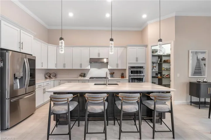 Kitchen featuring decorative backsplash, stainless steel appliances, crown molding, white cabinetry, and hanging pendants