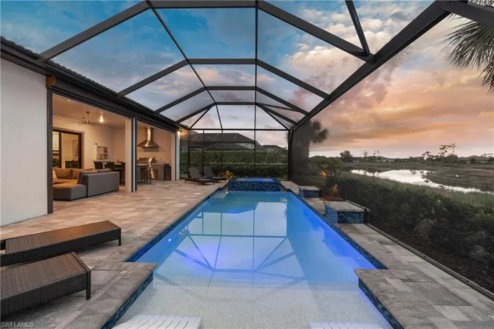 Pool at dusk with screen enclosure, a patio area, and a pool with connected hot tub