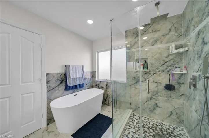Bathroom with a soaking tub, tile walls, a marble finish shower, marble tiled flooring, and a wainscoted wall