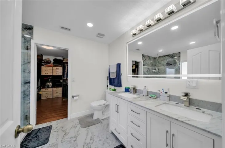 Bathroom featuring a marble finish shower, a walk in closet, light marble finish flooring, double vanity, and recessed lighting