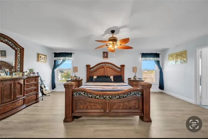 Bedroom with a ceiling fan, light wood-style flooring, and multiple windows