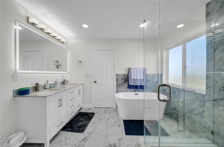 Bathroom with a soaking tub, double vanity, light marble finish flooring, a marble finish shower, and recessed lighting