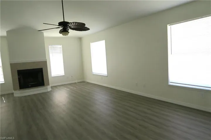 Unfurnished living room featuring a tiled fireplace, plenty of natural light, dark wood-type flooring, and a ceiling fan