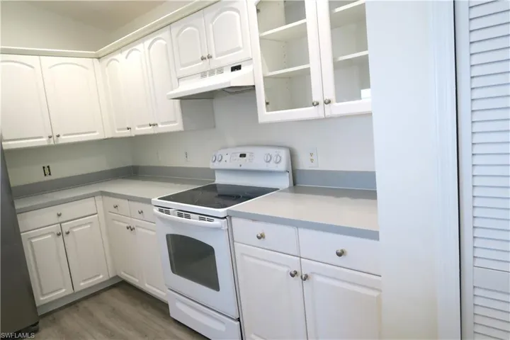 Kitchen with electric range, white cabinetry, under cabinet range hood, and light countertops