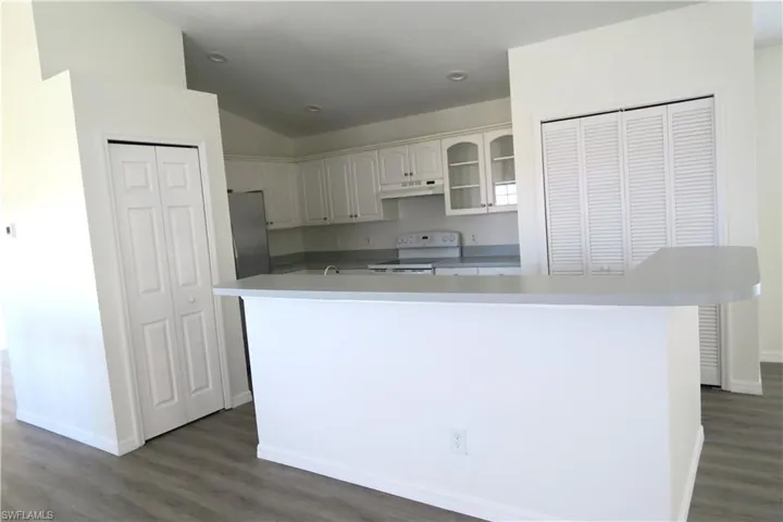 Kitchen with white cabinets, white range with electric cooktop, dark wood-type flooring, glass insert cabinets, and a center island