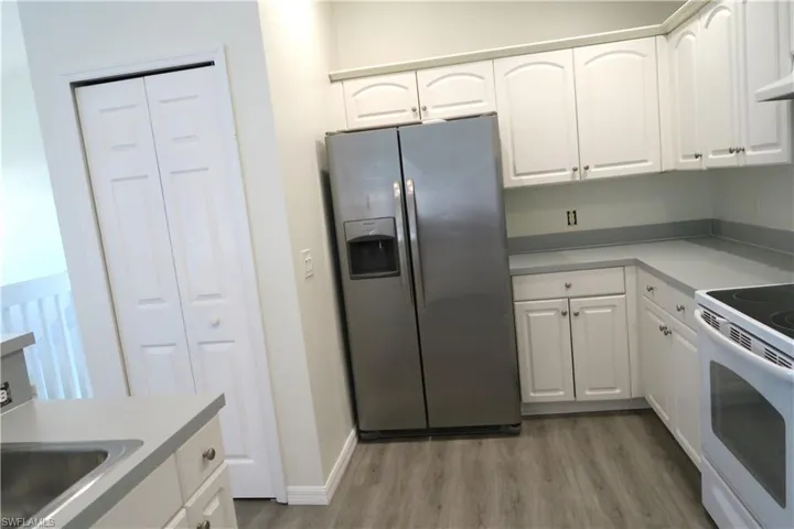 Kitchen featuring stainless steel fridge with ice dispenser, white cabinets, white electric range, light countertops, and light wood-style flooring