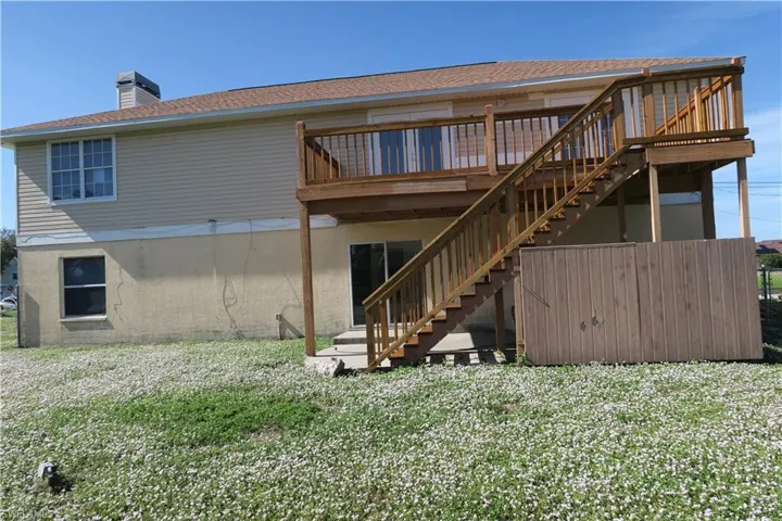 Back of house featuring a lawn, a chimney, stairs, roof with shingles, and a wooden deck
