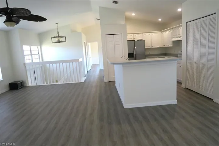Kitchen with lofted ceiling, stainless steel fridge with ice dispenser, a center island with sink, light countertops, and white cabinets