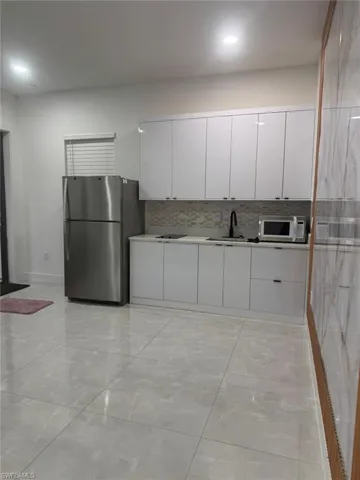 Kitchen with white cabinets, freestanding refrigerator, modern cabinets, and white microwave