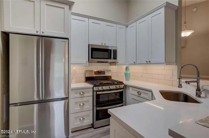 Kitchen featuring appliances with stainless steel finishes, tasteful backsplash, sink, light hardwood / wood-style floors, and decorative light fixtures