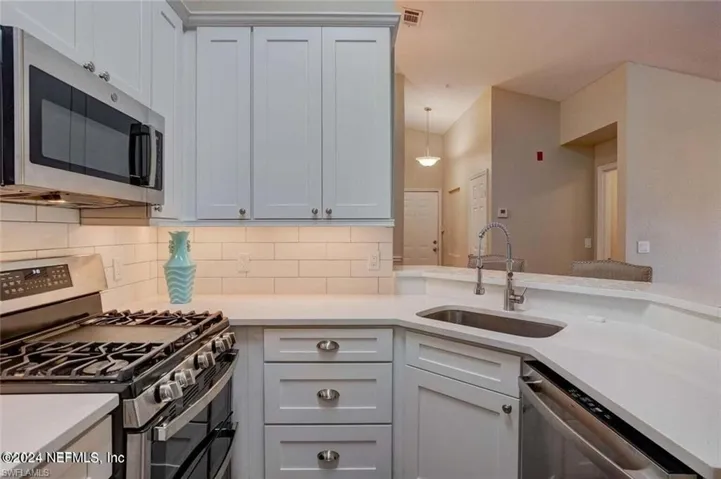 Kitchen featuring tasteful backsplash, white cabinets, stainless steel appliances, pendant lighting, and sink